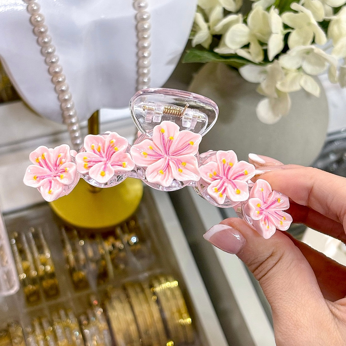 Pink Sakura Dream Clip with floral embellishments, held in a manicured hand.