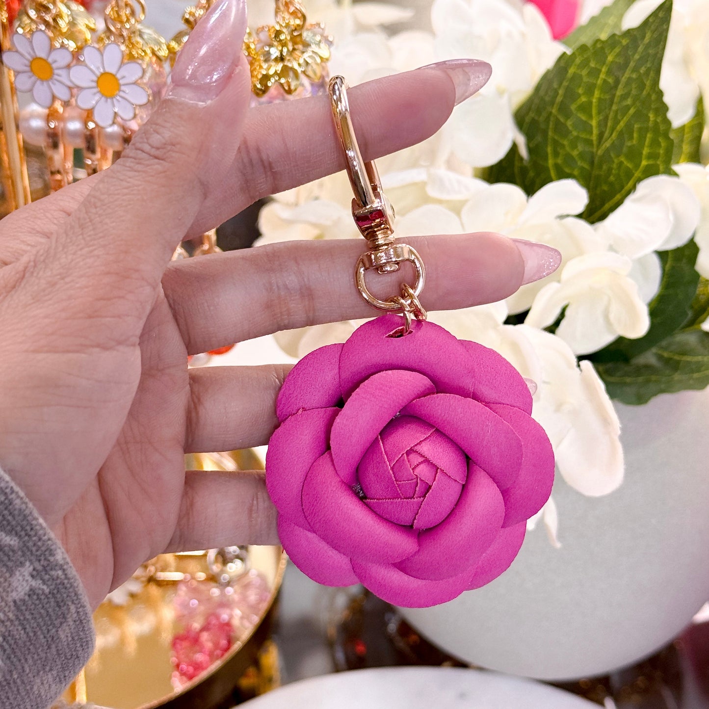 Pink rose bag charm from Valentine's Day Collection, held in hand with elongated nails and white floral background.