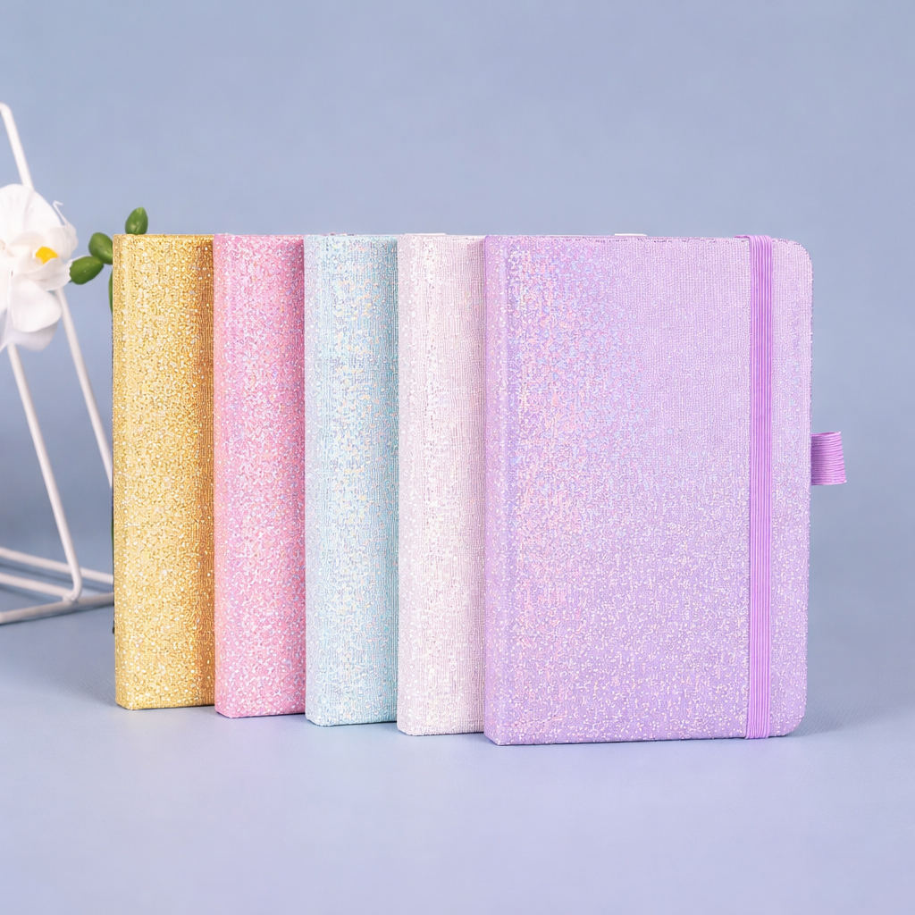 Five sparkly A5 journals in gold, pink, light blue, pale iridescent, and lavender, standing in a row, with elastic bands and ribbon markers.