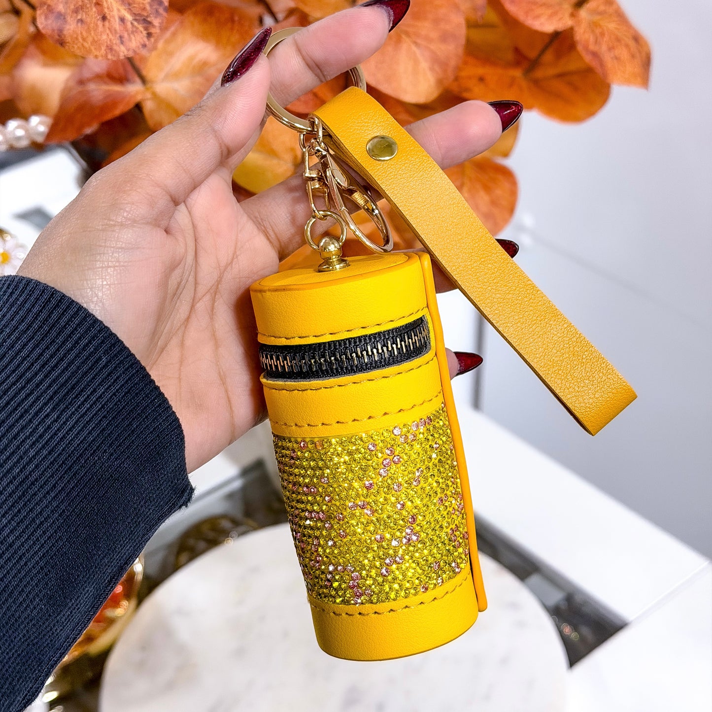 Yellow keychain with rhinestone details held by a hand against a blurred background