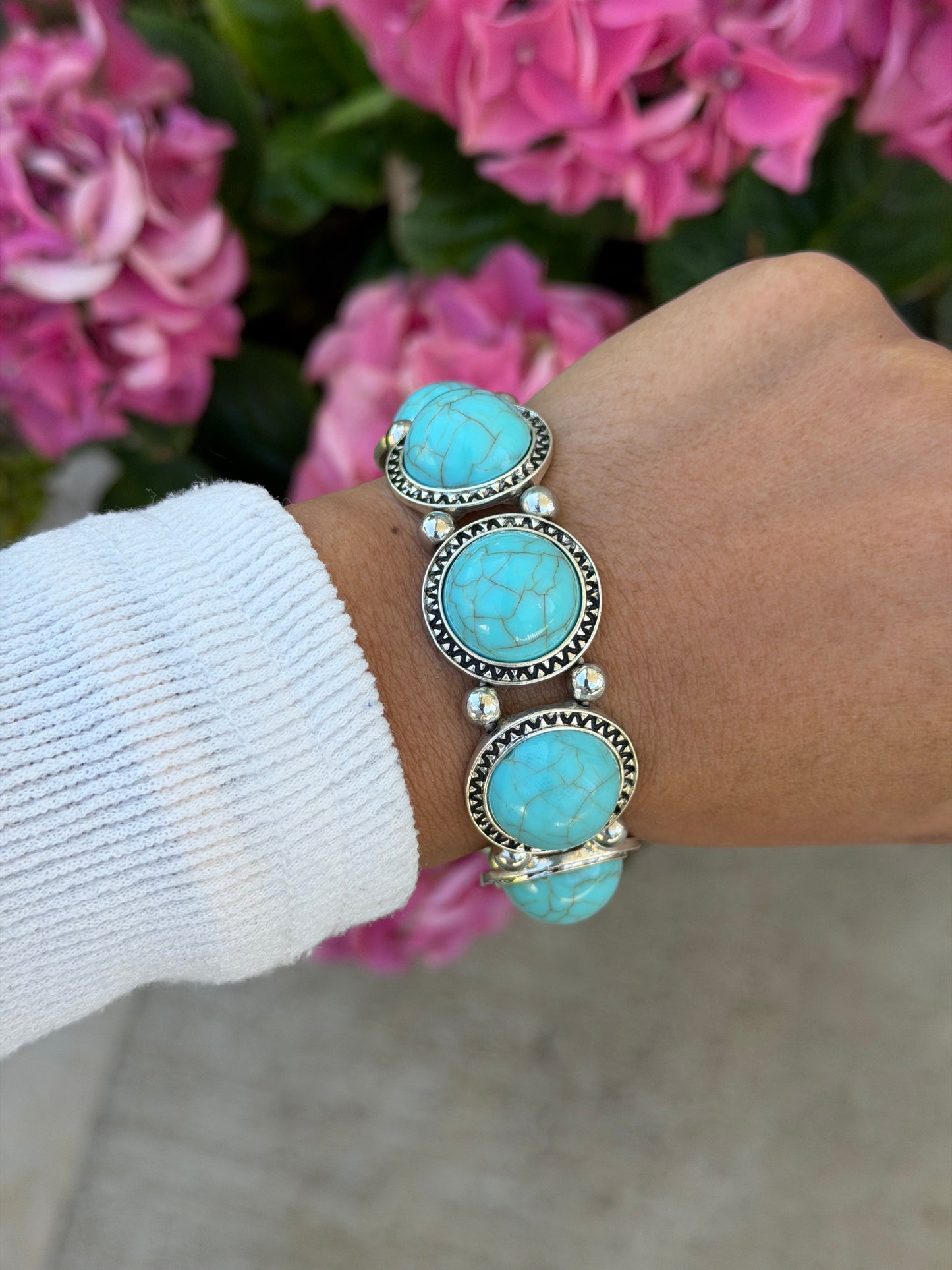 Chunky boho bracelet with cracked turquoise-look stones in silver-tone settings worn on a wrist with a white sweater.
