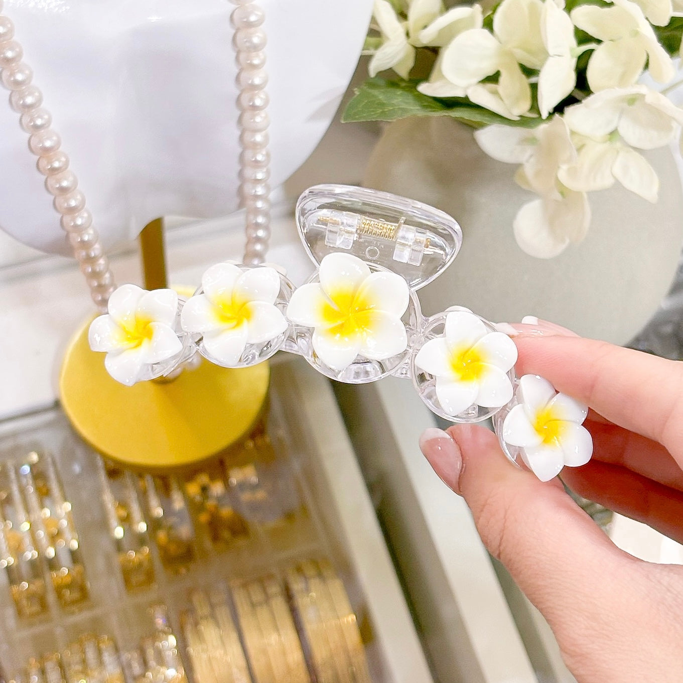Clear hair claw with white and yellow flower accents, featuring frangipani detailing.