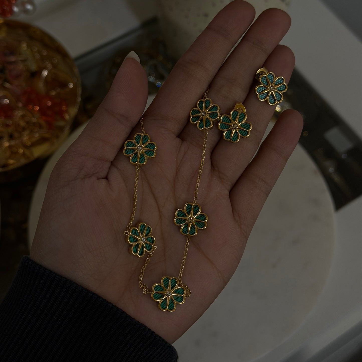 Gold necklace with green floral pendants held in a hand against a blurred background