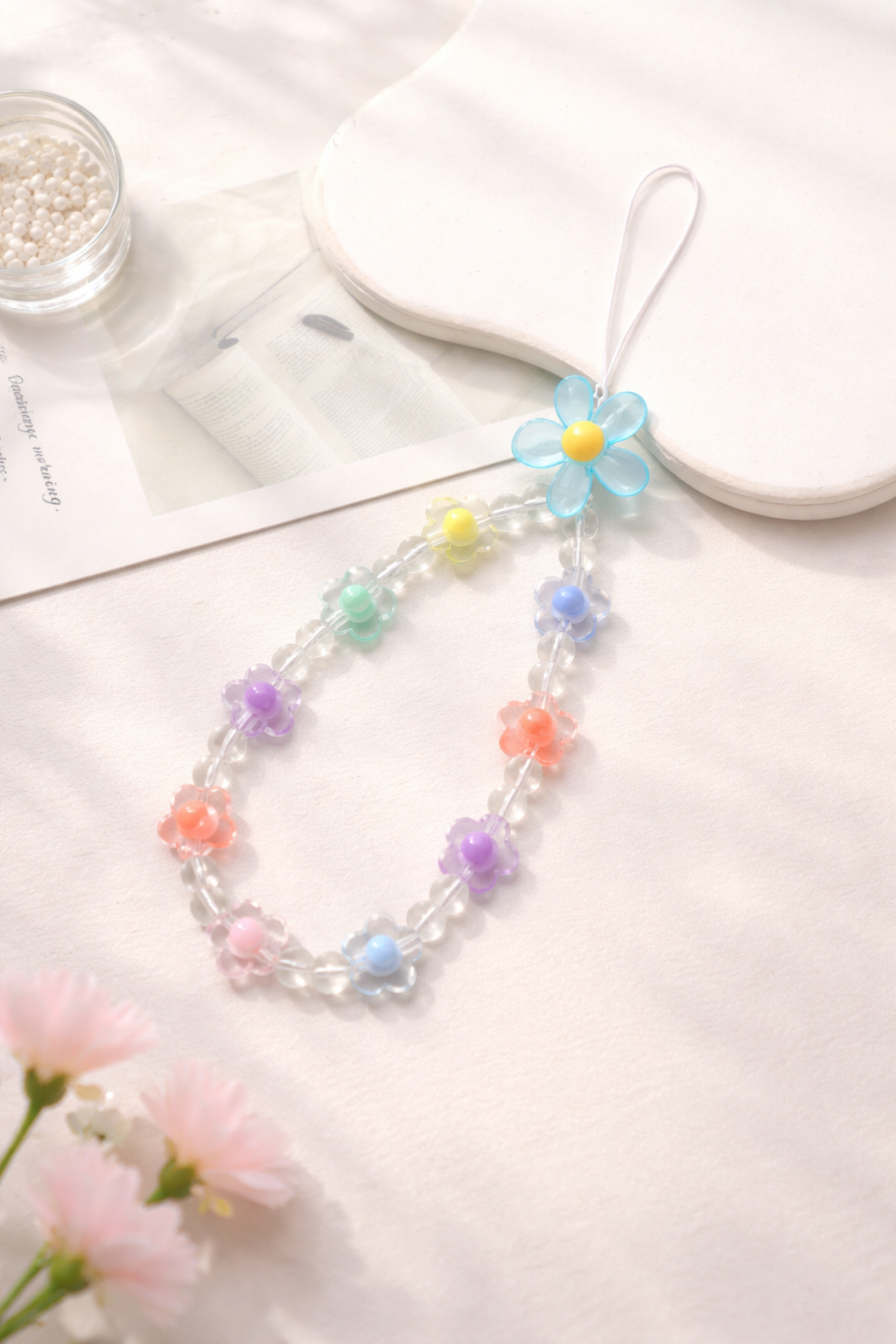 Colorful phone strap with clear and pastel daisy-shaped beads, displayed on a textured white surface.