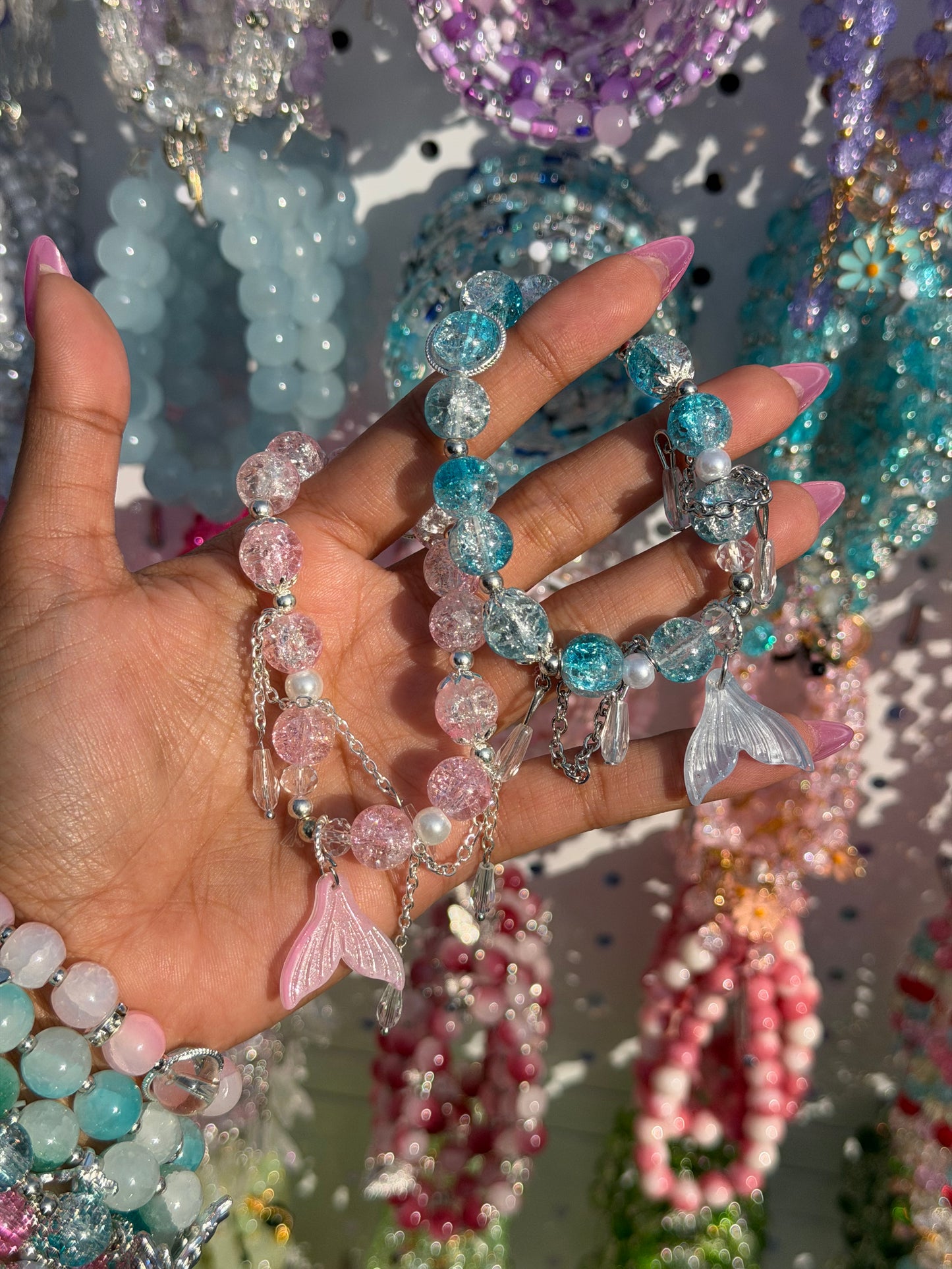 Mermaid Charm Beaded Bracelet with pink, blue, and clear cracked glass beads, silver accents, and two translucent mermaid tails, held in a hand.