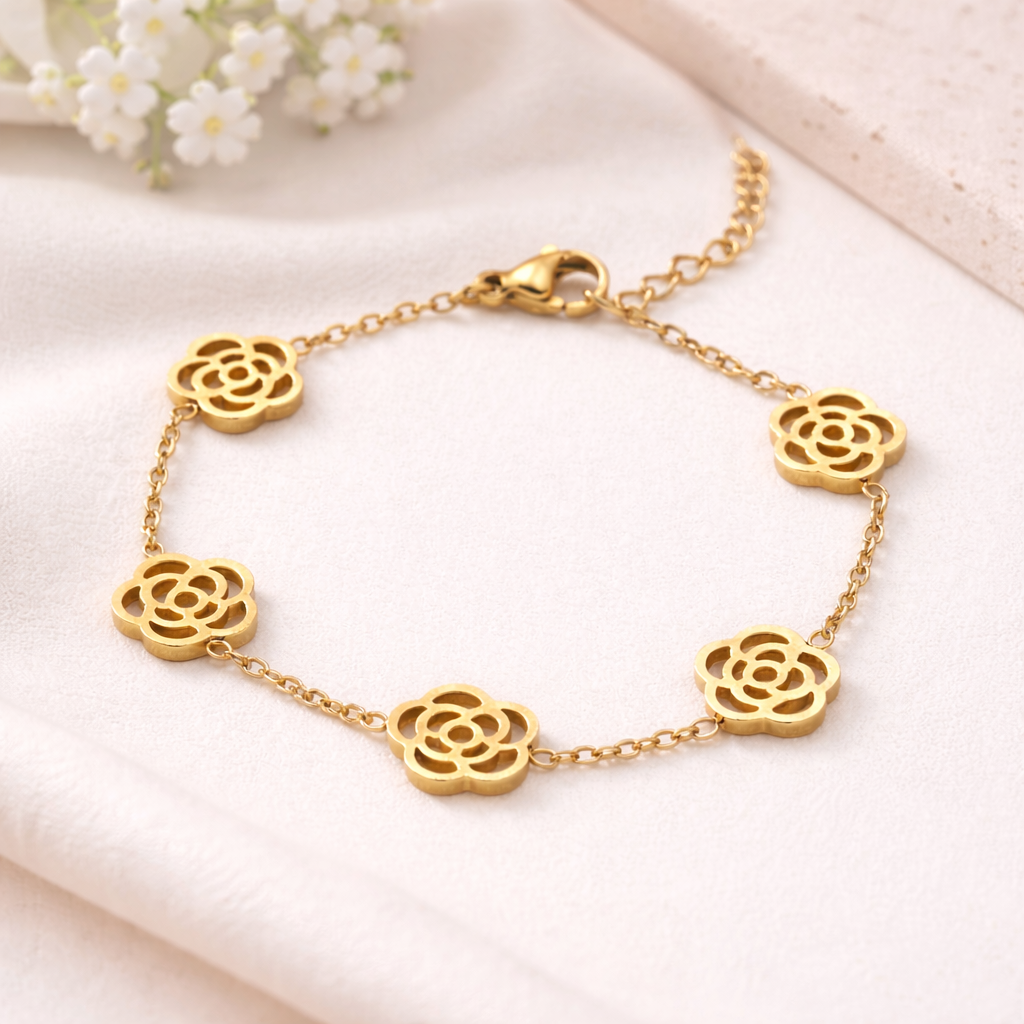 Gold rose bracelet with five openwork flower charms and a delicate chain, resting on a white fabric.
