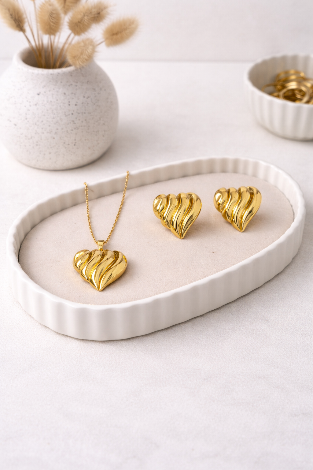 Gold fluted heart necklace and matching earrings set, displayed on a light beige tray.