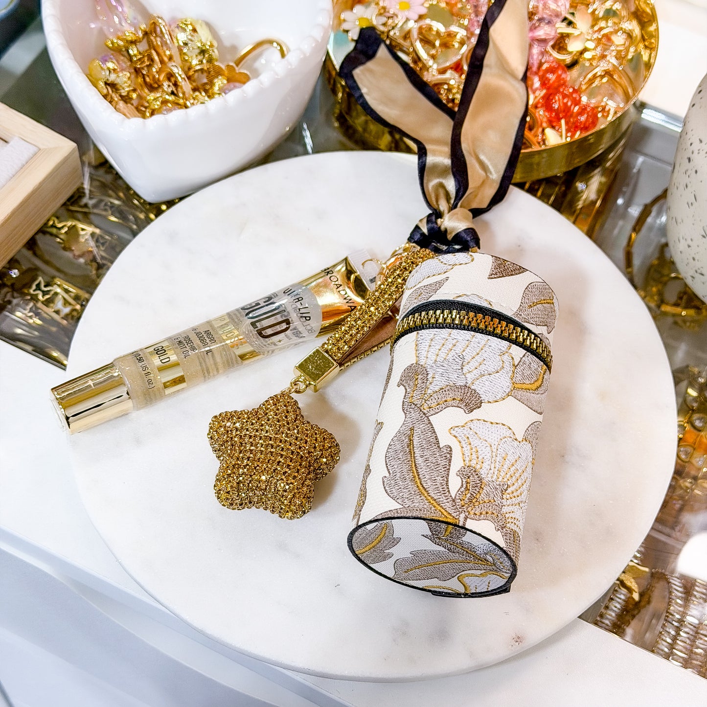 Cream floral coin purse combo set with zippered coin pouch, clear gold-tinted lip gloss, and star-shaped rhinestone keychain displayed on a white marble plate.