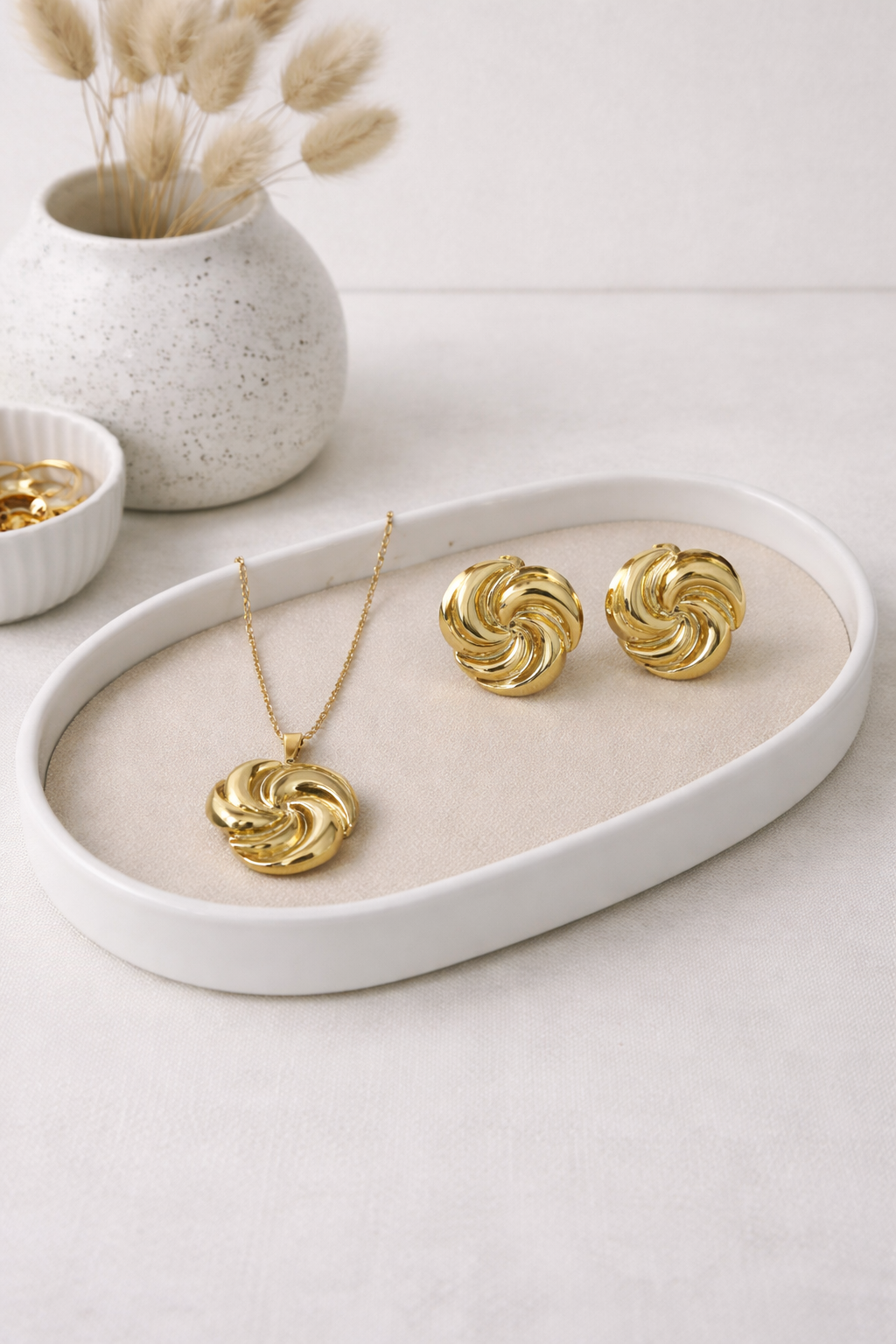 Gold swirl necklace and matching earrings set on a beige display tray.