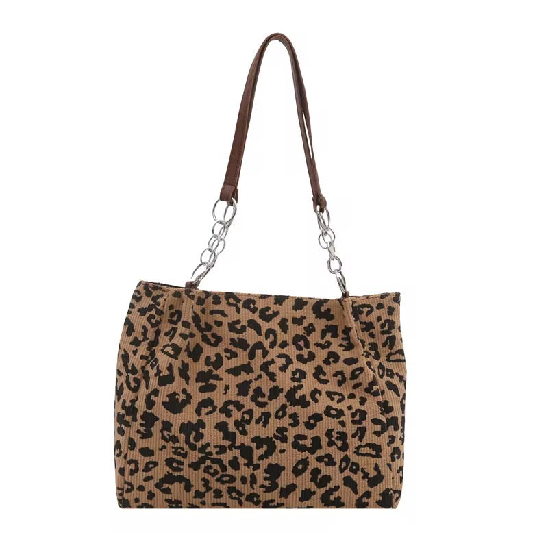 Leopard shoulder bag with brown handles and silver chain detail.