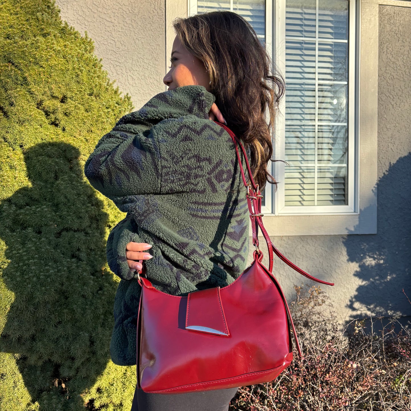 Red leather shoulder bag by unknown brand with a silver accent, worn with a patterned fleece jacket.