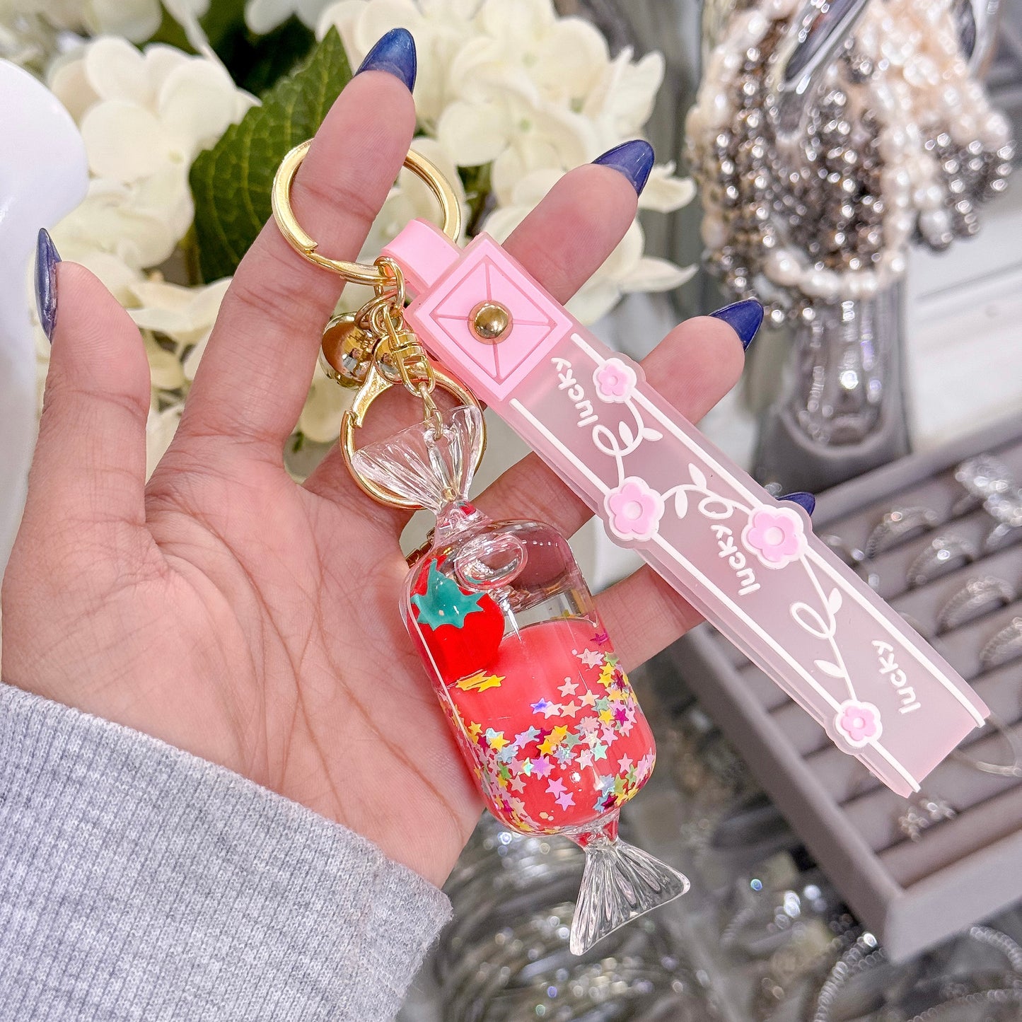 Strawberry bag charms with star confetti filling, by unknown brand, held in hand with blue nails.