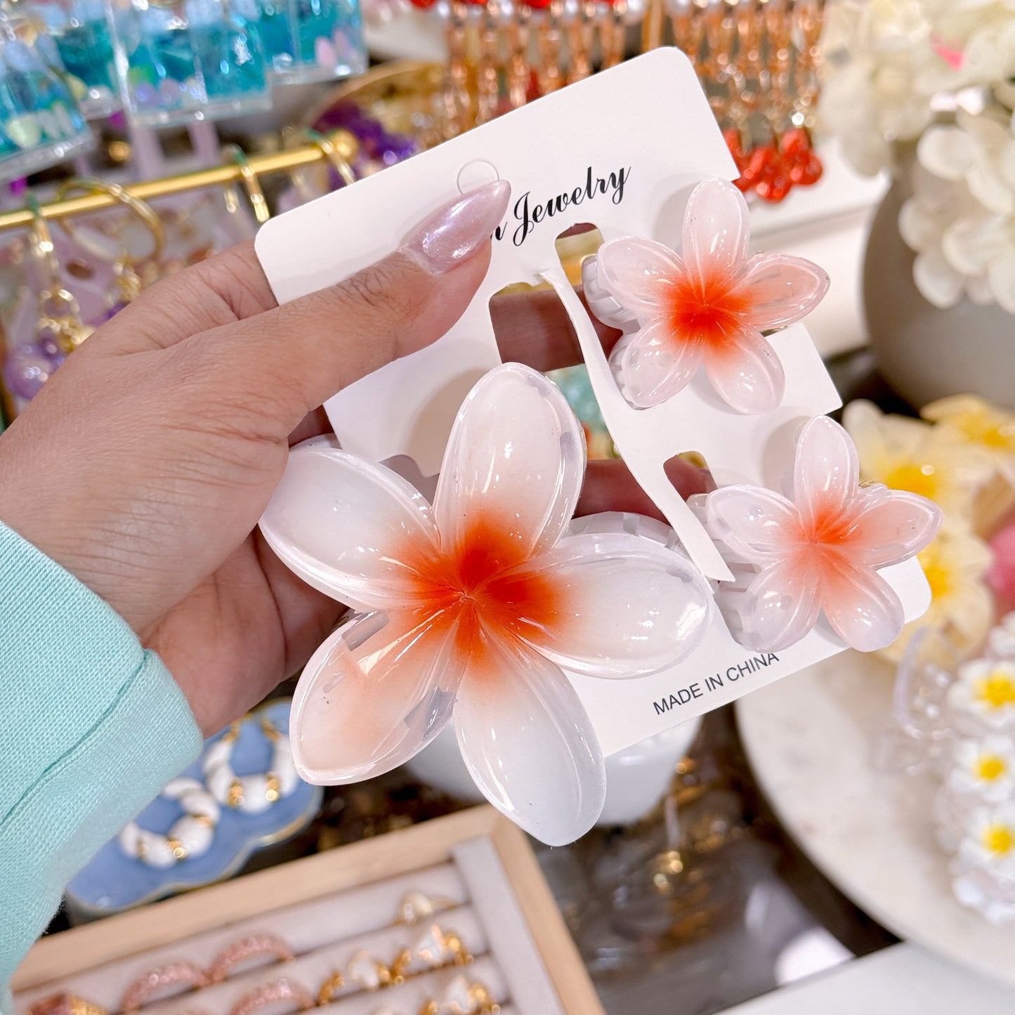 White plumeria hair clip set from "N Jewelry," featuring an orange center, attached to a display card.