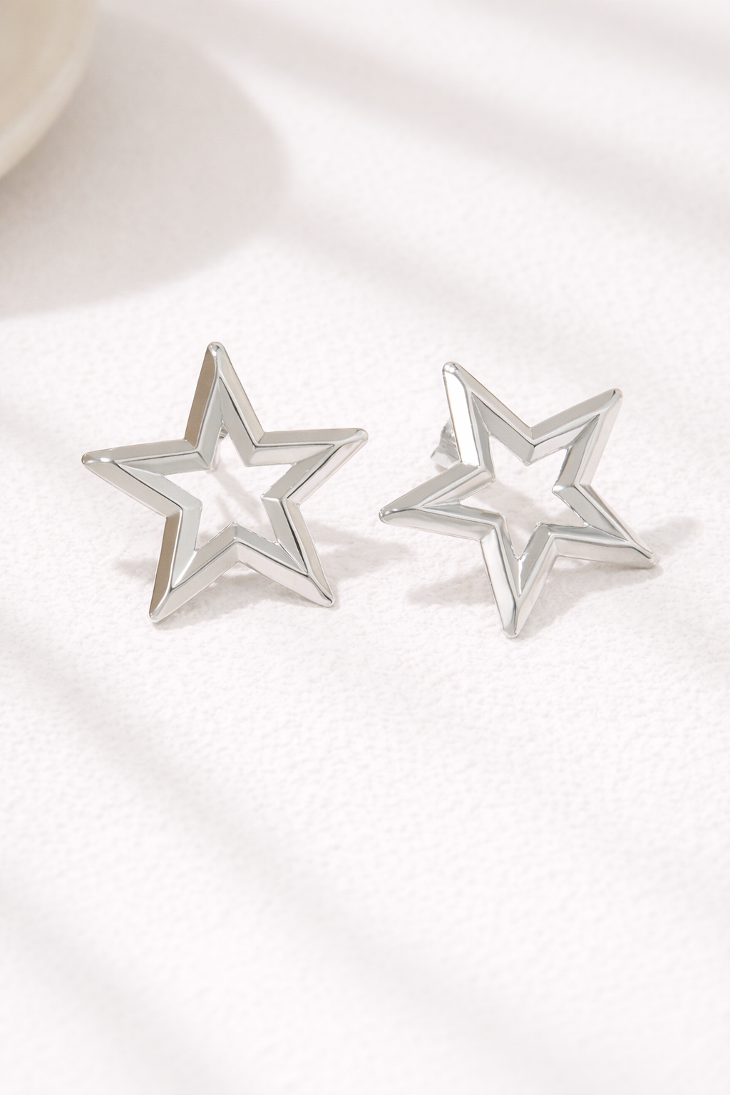 Two silver star-shaped hollow stud earrings with a polished finish, on a textured white surface.