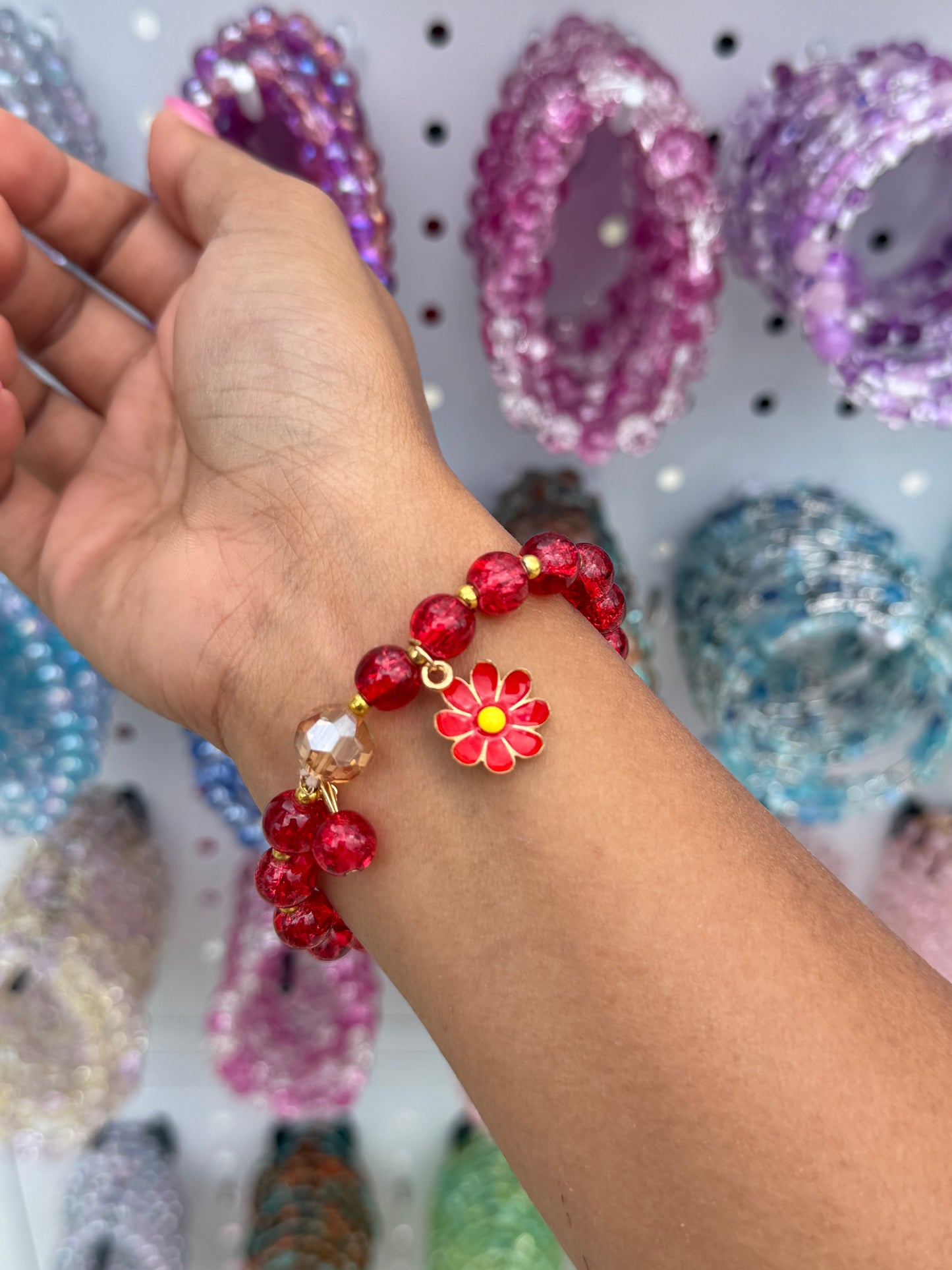 Red daisy beaded bracelet featuring translucent red beads and a red flower charm with a yellow center, worn on an arm.