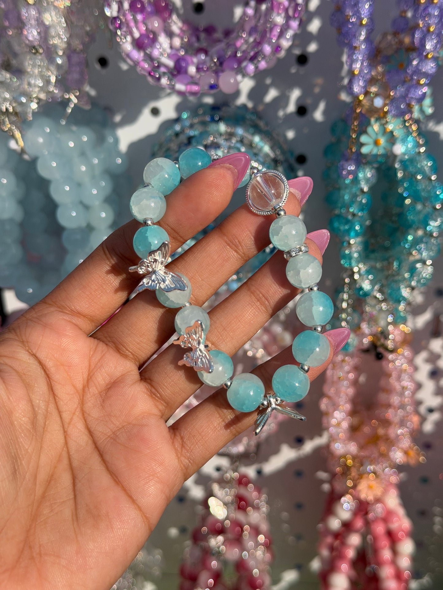 Light blue beaded bracelet with silver butterfly charms and a clear bead, worn on a hand with pink nails.