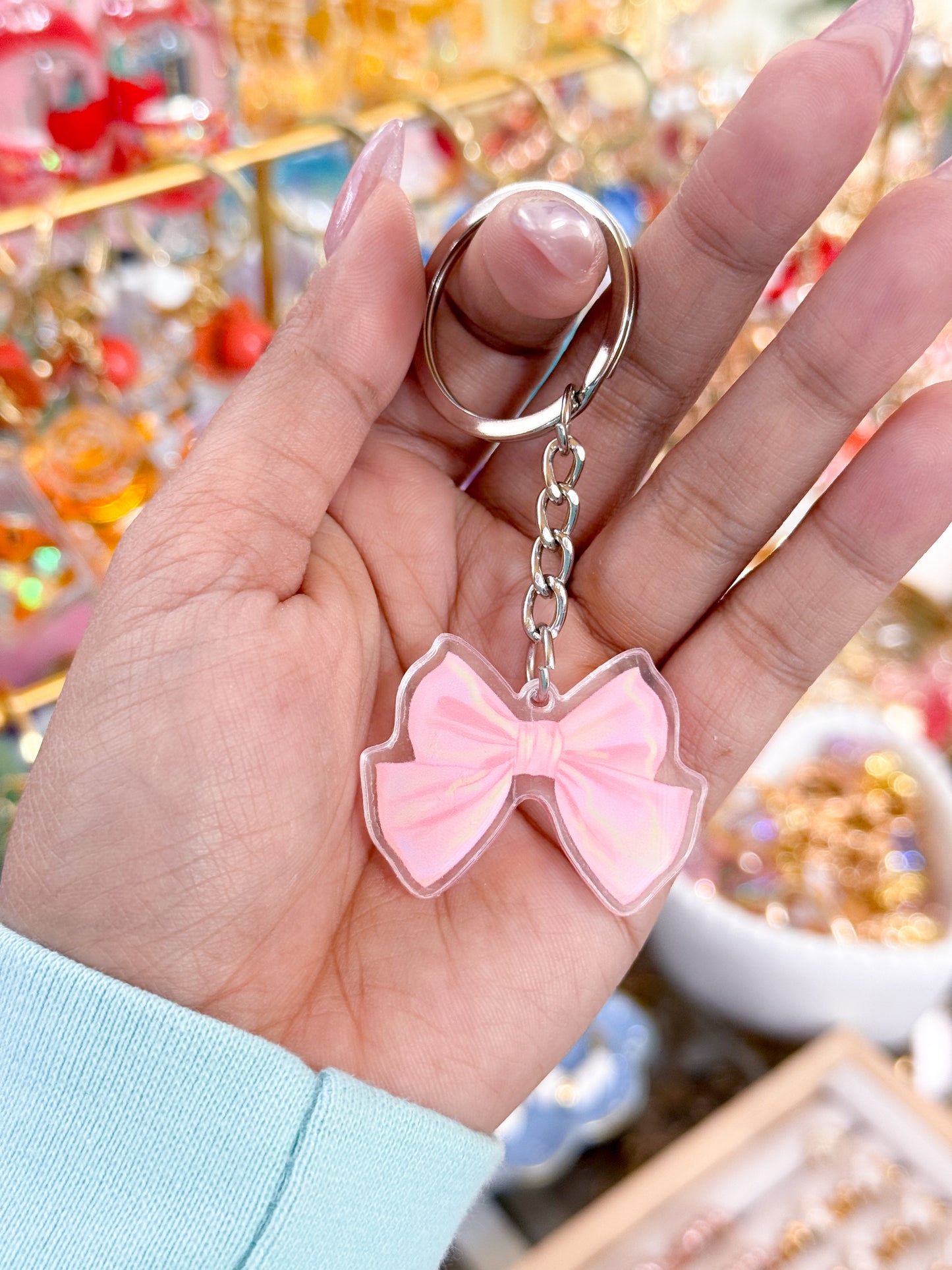 Pink bow keychain by an unknown vendor, hanging from a silver keyring with a chain, and clear edges.