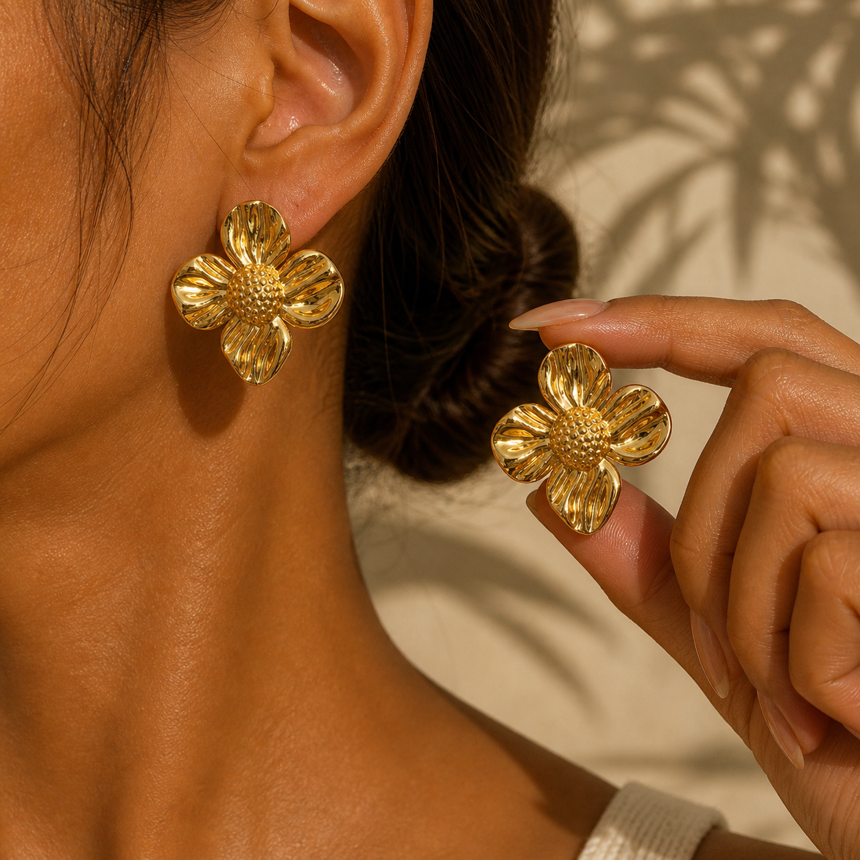 Gold-toned chunky sunflower earrings with ridged petals, one worn on an ear, one held by fingers.