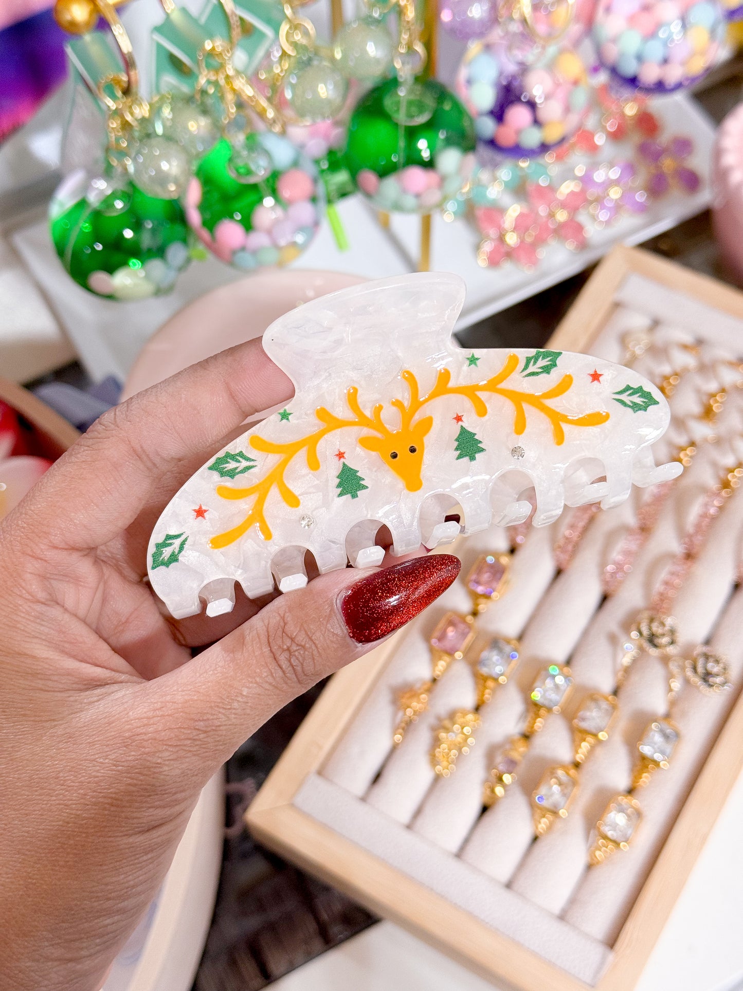 White reindeer hair claw clip with holiday design, featuring orange reindeer by an unknown vendor, with green Christmas trees and red stars.