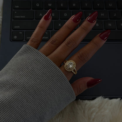 Gold oval halo ring with pavé-set band, worn on hand.