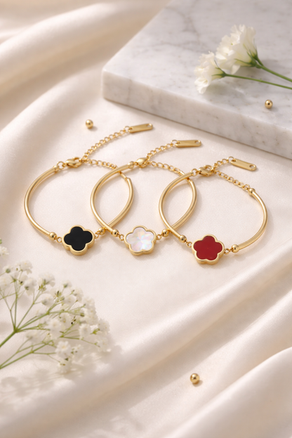 Three gold-tone Abigail bracelets with black, iridescent white, and red clover charms on white satin.