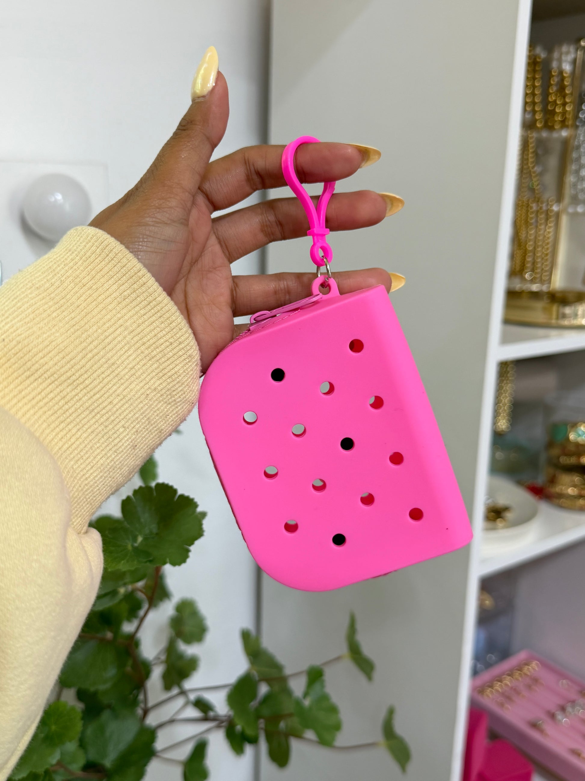 Pink silicone charm pouch with circular holes, held by a hand in a yellow sweater with yellow nails.