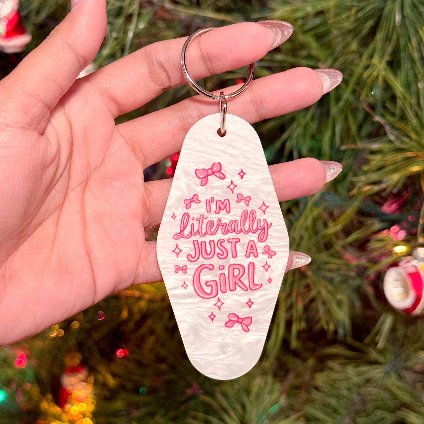White motel keychain with pink lettering and bow graphics, held in hand.