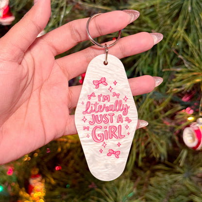 White motel keychain with pink lettering and bow graphics, held in hand.