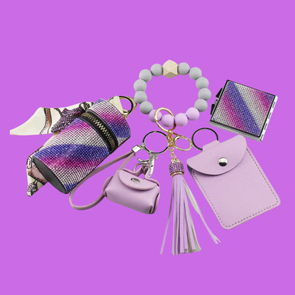 Purple Luxe keychain wristlet accessory set featuring a beaded wristlet, rhinestone zip pouch, mini pouch, tassel charm, card holder, and sparkly compact mirror in coordinating colors.