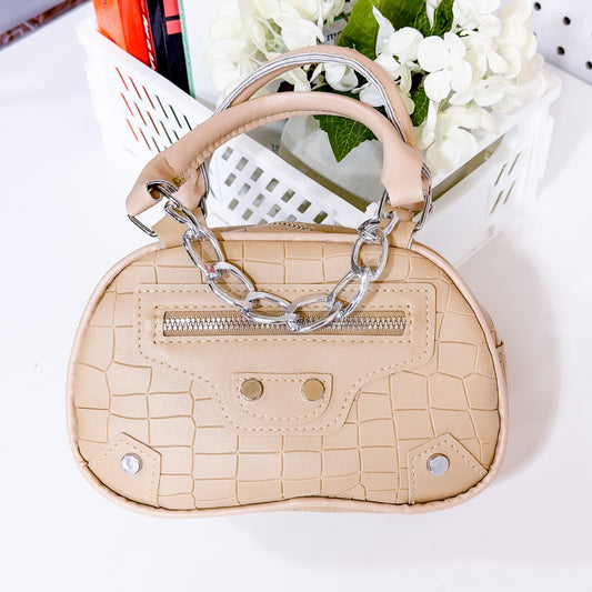Beige handbag with clear chain handle on a white surface with flowers in the background
