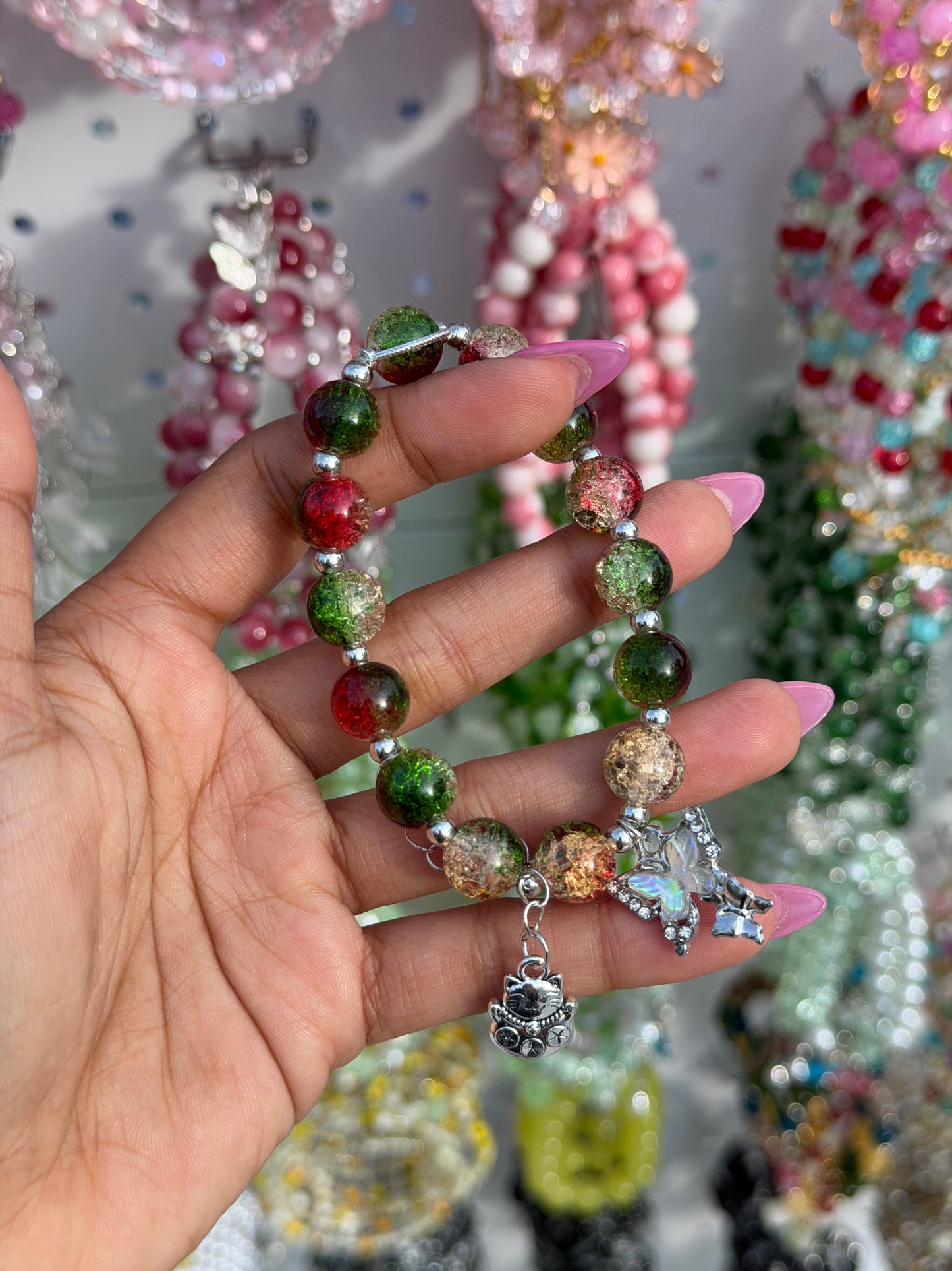 Green, red, and clear crackle beaded bracelet with butterfly and lucky cat charms, held by a hand.