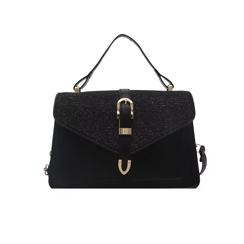 Black shoulder bag by The Uptown, featuring a buckle closure, a top handle, and gold-toned hardware.