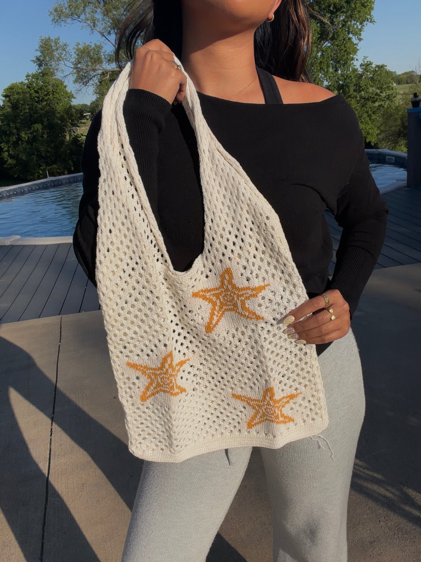 Off-white mesh knit bag featuring orange starfish, carried on a person's shoulder.