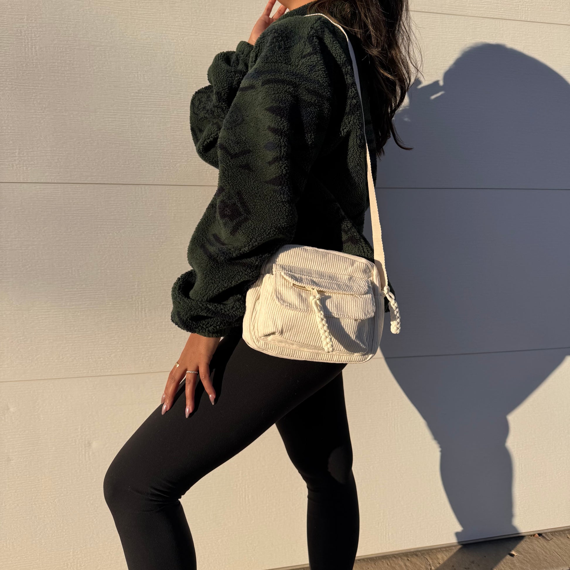 White corduroy crossbody bag with pockets, shown with black leggings and a dark patterned fleece top.