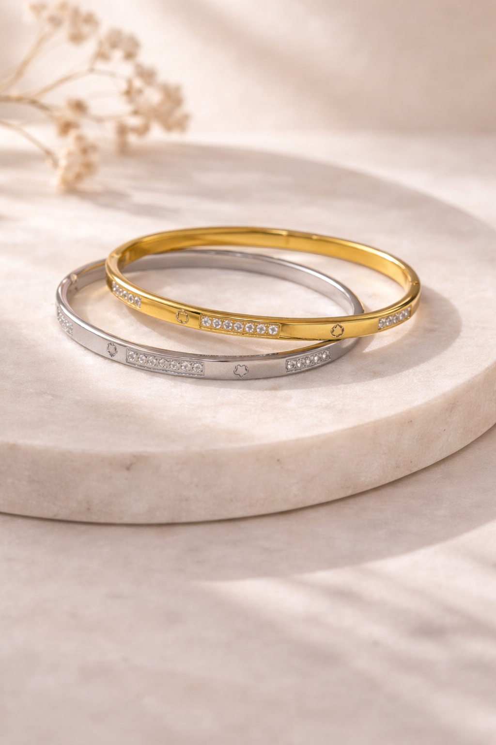 Gold and silver Sparkle Sweetheart Bangle bracelets featuring crystal accents and small symbols, stacked on a white marble surface.