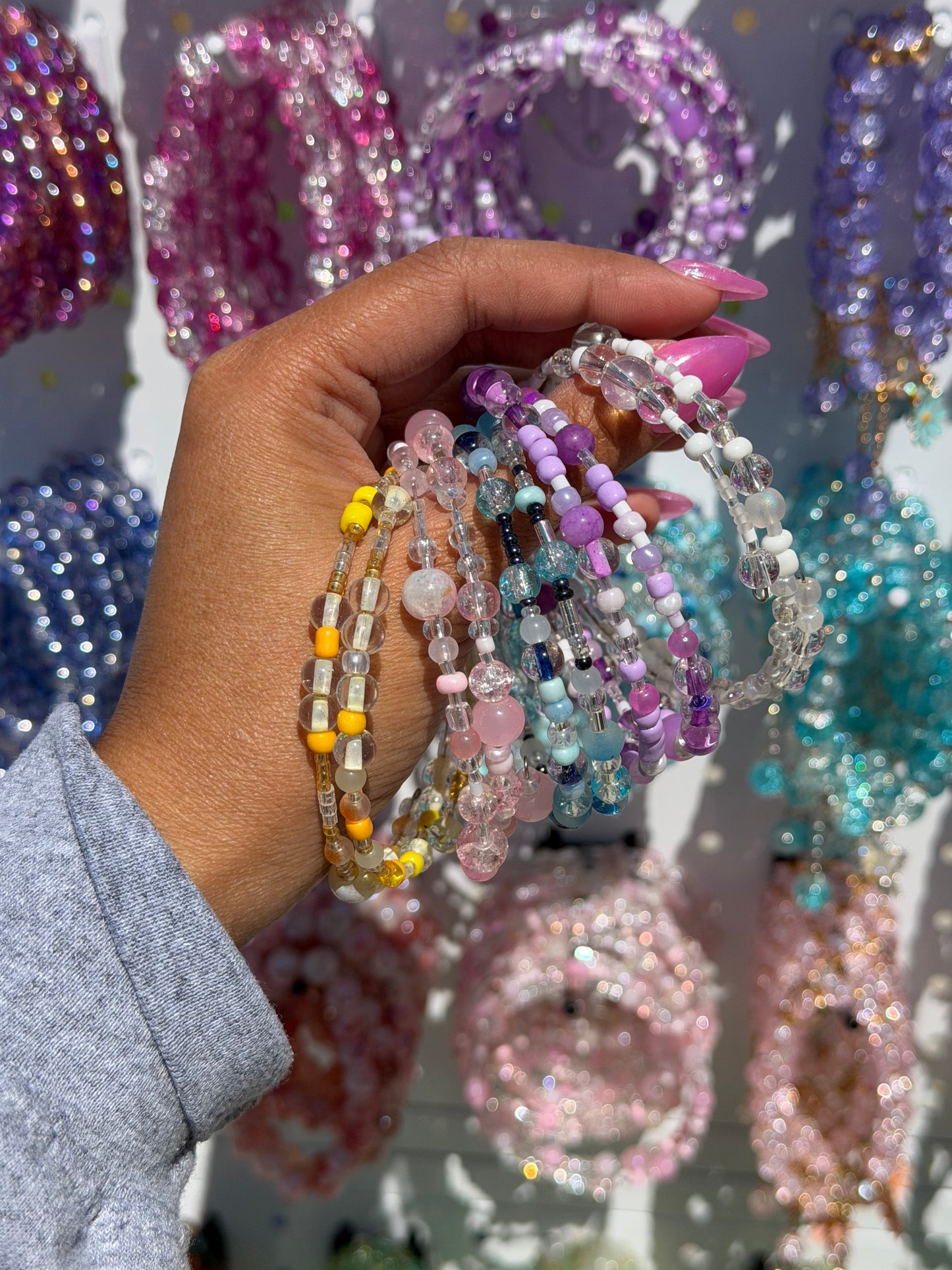Layered beaded bracelets with yellow, pink, clear, purple, blue, and white beads held by a hand with pink nails.