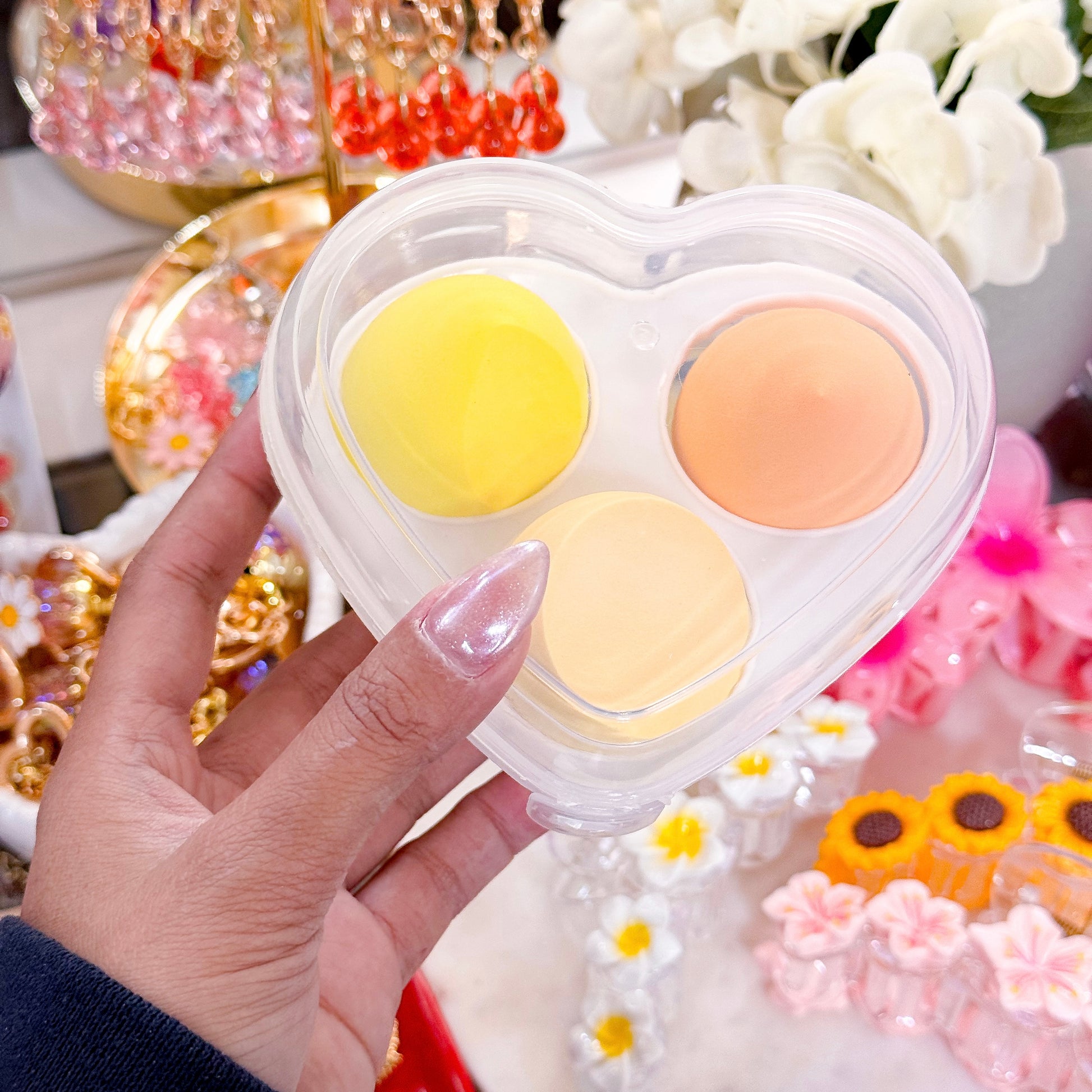 Cosmetic sponges in a heart-shaped plastic case, featuring yellow and orange hues, held in hand.