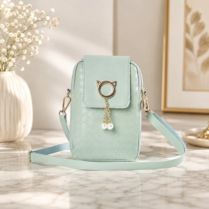 Mint green woven phone crossbody pouch featuring a gold cat head ring with hanging pearl charms, on a marble surface.