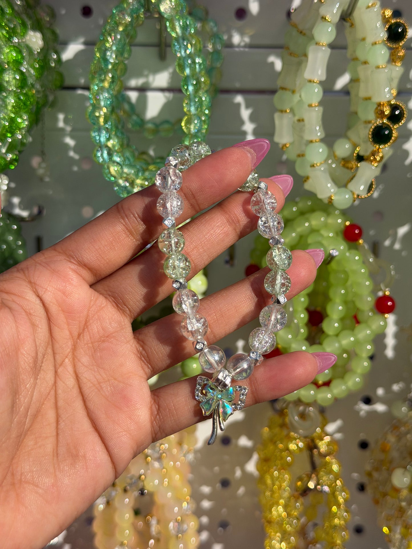 Green Lucky Charms Beaded Bracelet with clear and light green cracked beads and an iridescent butterfly charm, held by a manicured hand.
