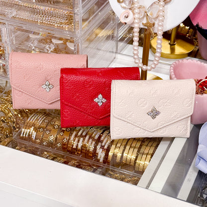 Assorted short wallets with flap, by Belle, including pink, red, and cream colors with decorative floral embossed pattern.