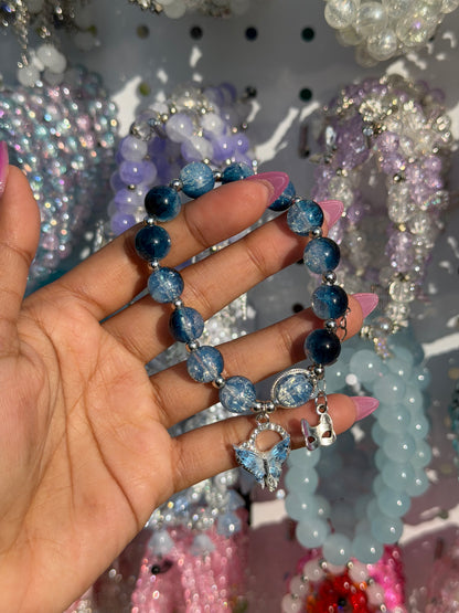 Blue Butterfly Charm Beaded Bracelet with mixed blue beads, a silver mask charm, held by a hand with pink nails.