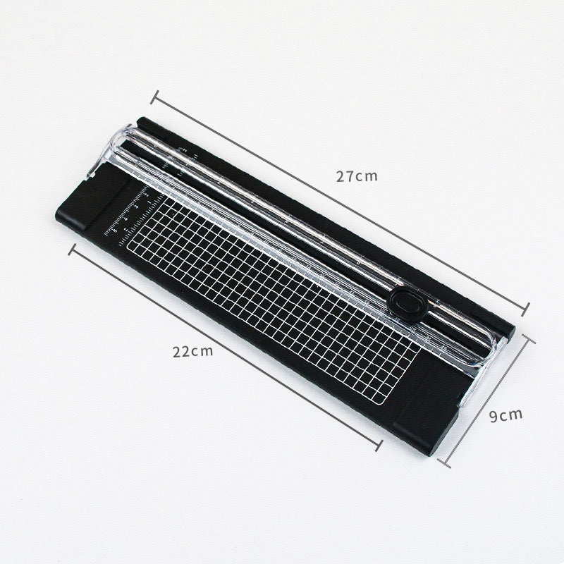 Black plastic paper and photo cutter with clear sliding guide, white grid, and ruler, 27cm long, 9cm wide.