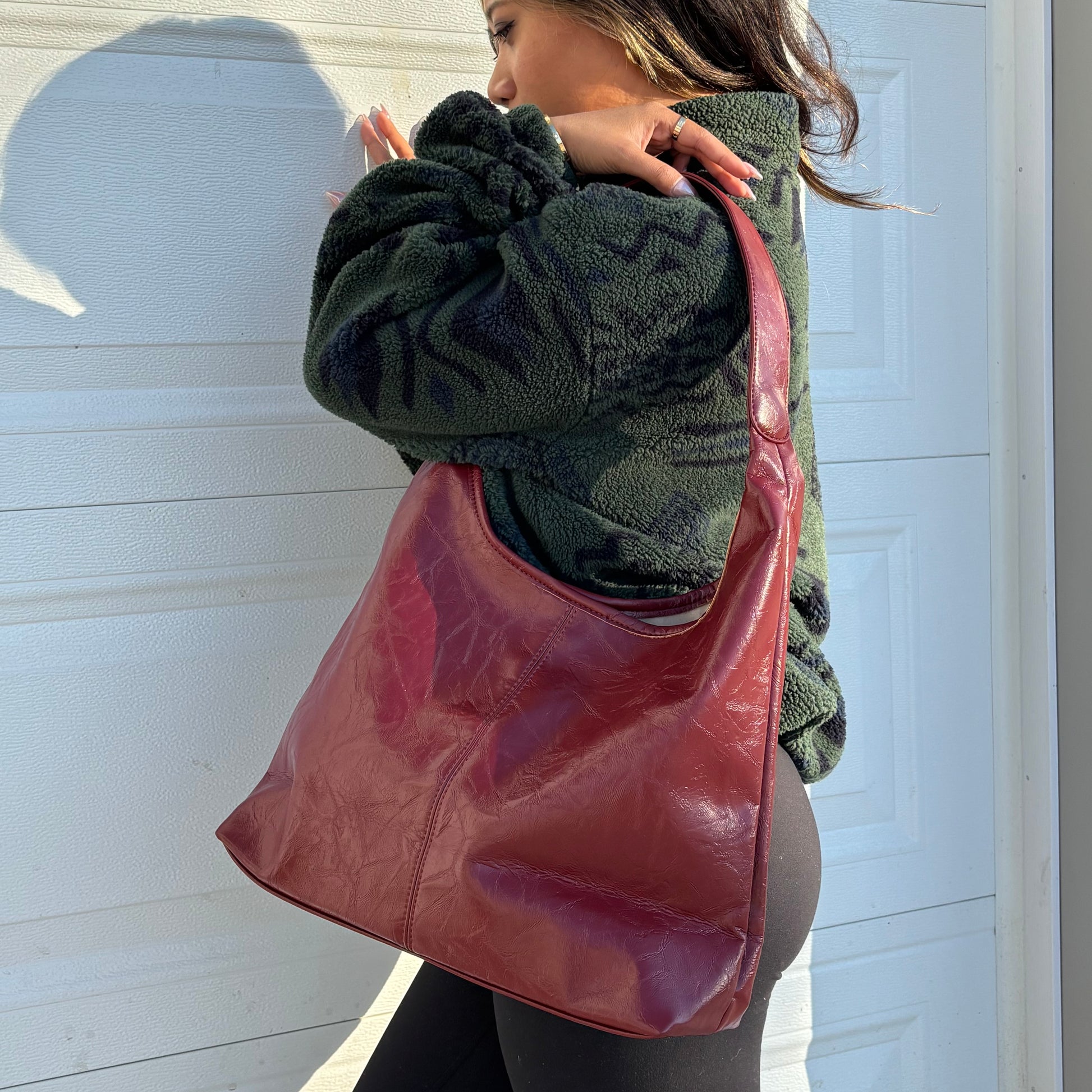 Red leather tote bag with top handle, against a white door with a textured green fleece jacket.