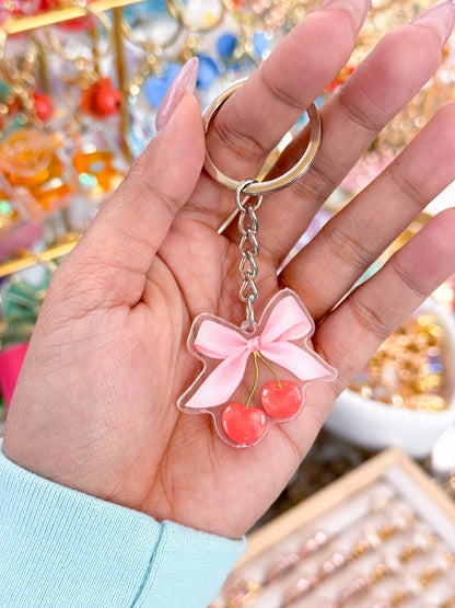 Acrylic cherry keychain with a pink bow by an unknown vendor, held in someone's palm.