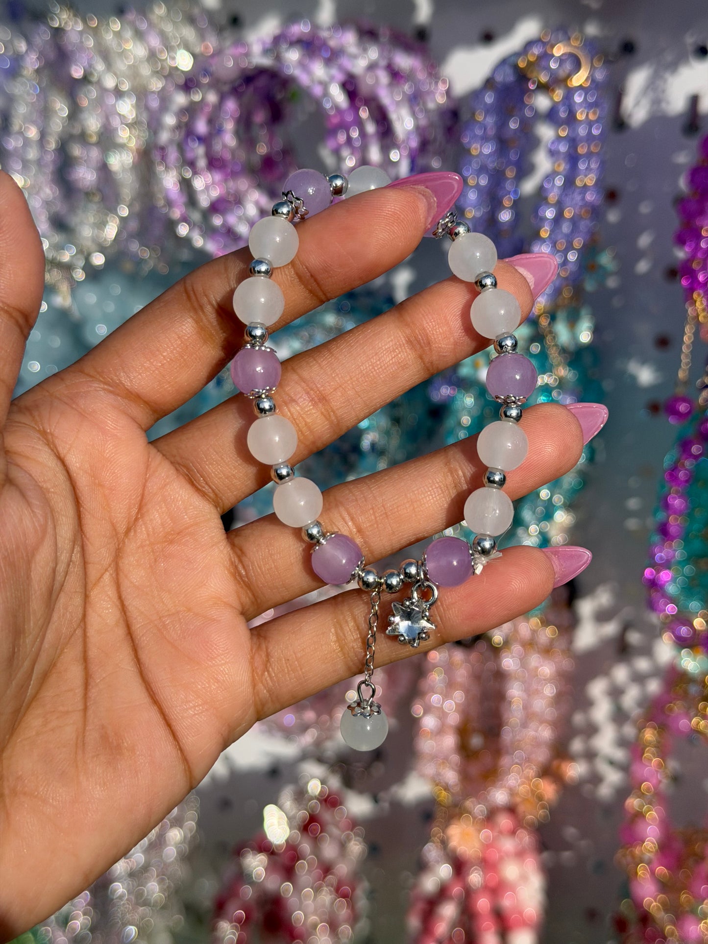 Lilac and white beaded bracelet with a star charm, held by a hand with pink nails.