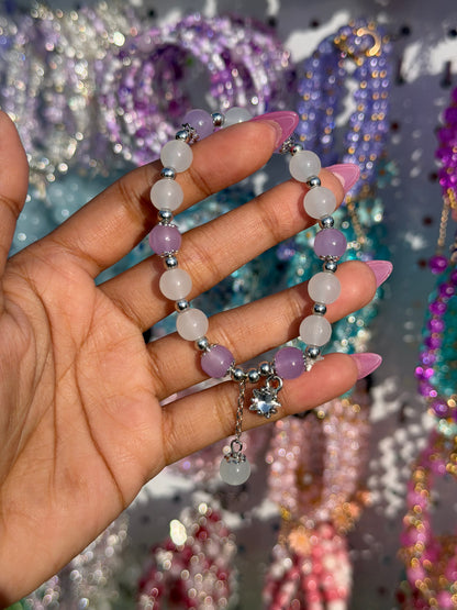 Lilac and white beaded bracelet with a star charm, held by a hand with pink nails.