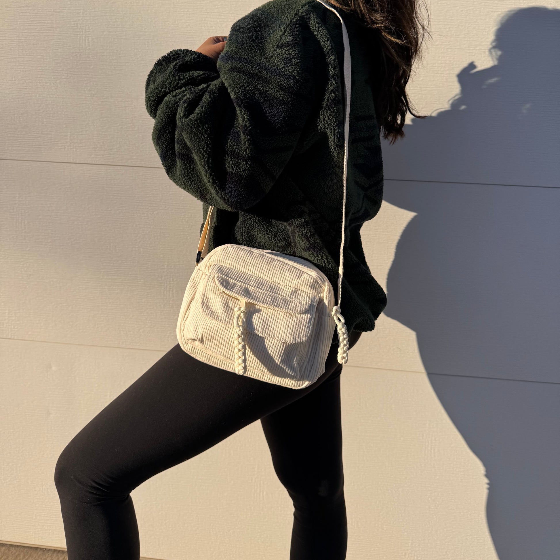 Cream corduroy crossbody bag from The Cozy Errands, featuring a zippered pocket with decorative cord accents, styled with leggings and a fleece jacket.