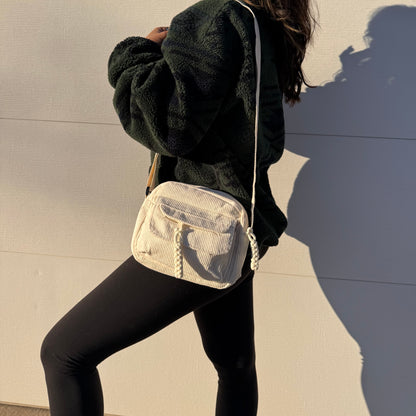Cream corduroy crossbody bag from The Cozy Errands, featuring a zippered pocket with decorative cord accents, styled with leggings and a fleece jacket.
