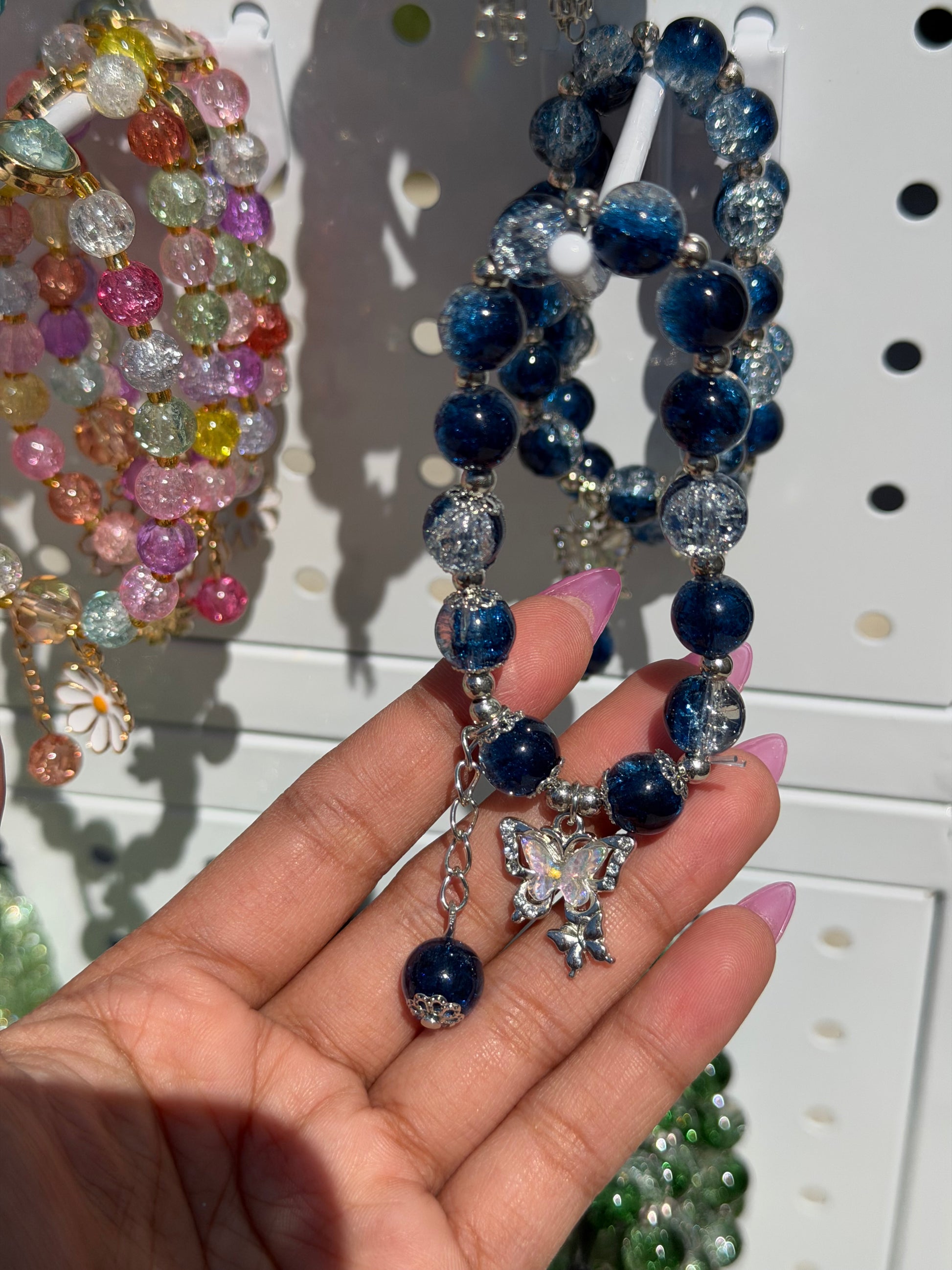 Blue beaded bracelet with dark and light blue crackle beads and a silver butterfly charm, held by a hand, displayed with colorful bracelets.
