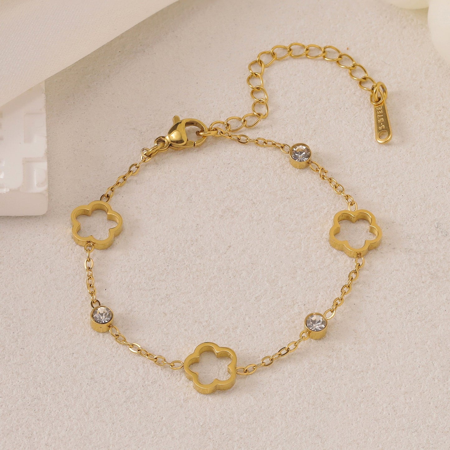 Gold-toned chain bracelet with open clover charms, clear cubic zirconia stones, and an 'S-STEEL' tag.